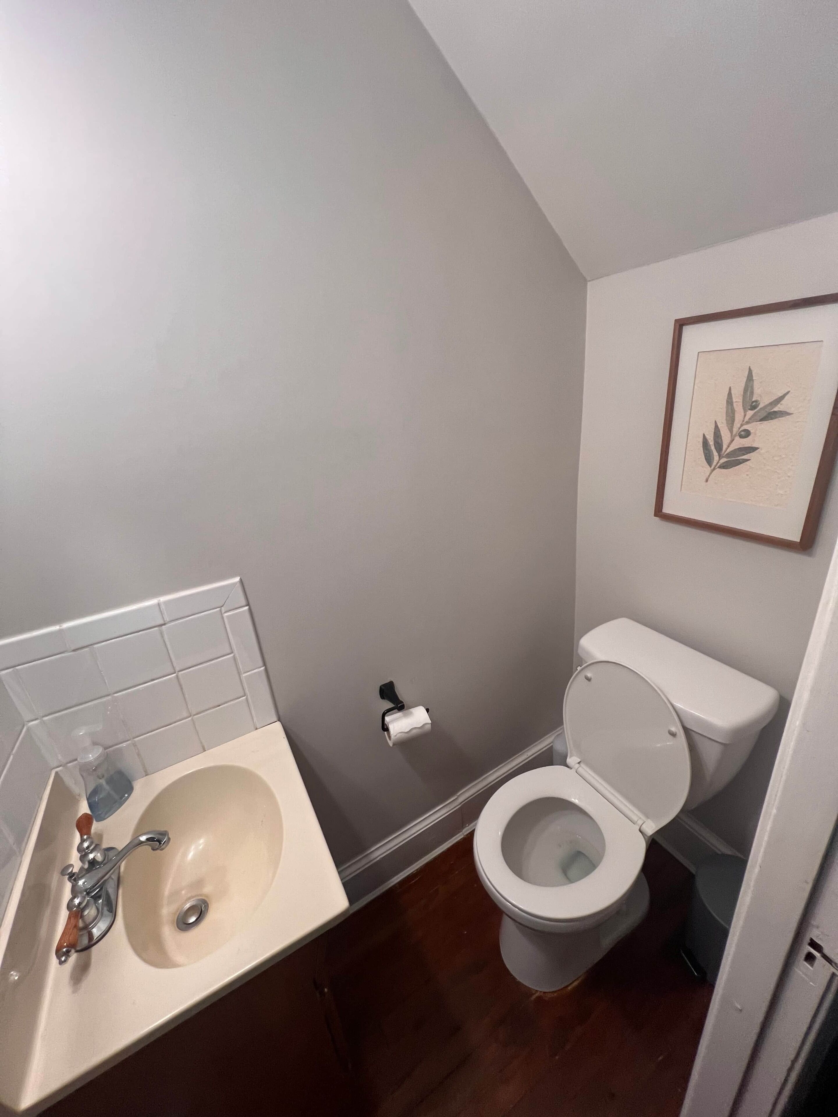 A bathroom with a sink, toilet, and a framed artwork on the wall.