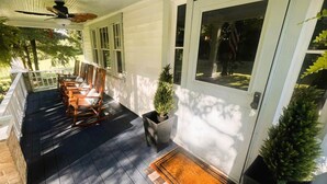 A porch with wooden rocking chairs, a potted plant, a doormat, and a ceiling fan.
