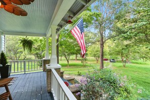 A covered porch with an American flag, a view of a green lawn, and a pathway.