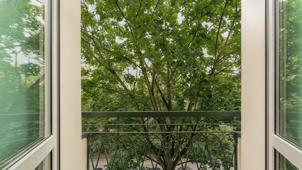 A balcony with a view of a tree and parked cars. - Grzegórzki Comfort Apartment (Kraków)