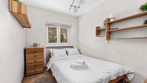 A bedroom with a bed, wooden dresser, window, and built-in shelves. - Grzegórzki Comfort Apartment (Kraków)