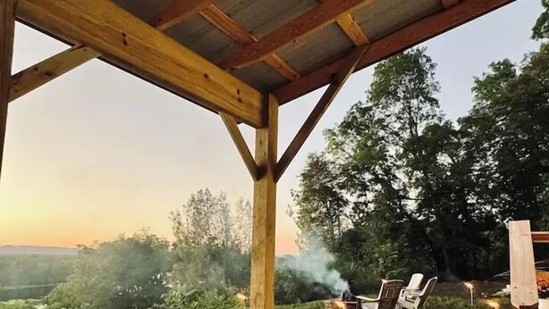 Kylpytynnyri puisen pergola-katoksen alla, josta avautuu näkymä maaseudulle.