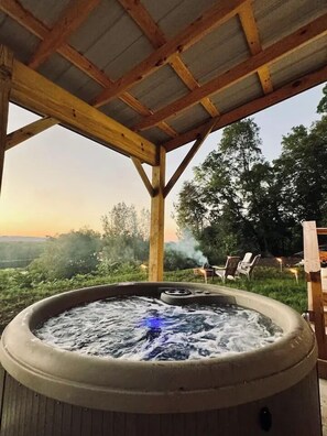 A hot tub under a wooden pergola with a view of the countryside.