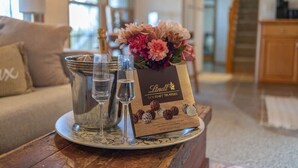 Puisella pöydällä on tarjotinalusta, jonka päällä on samppanjapullo, lasit ja pakkaus Lindt Gourmet -tryffeleitä.