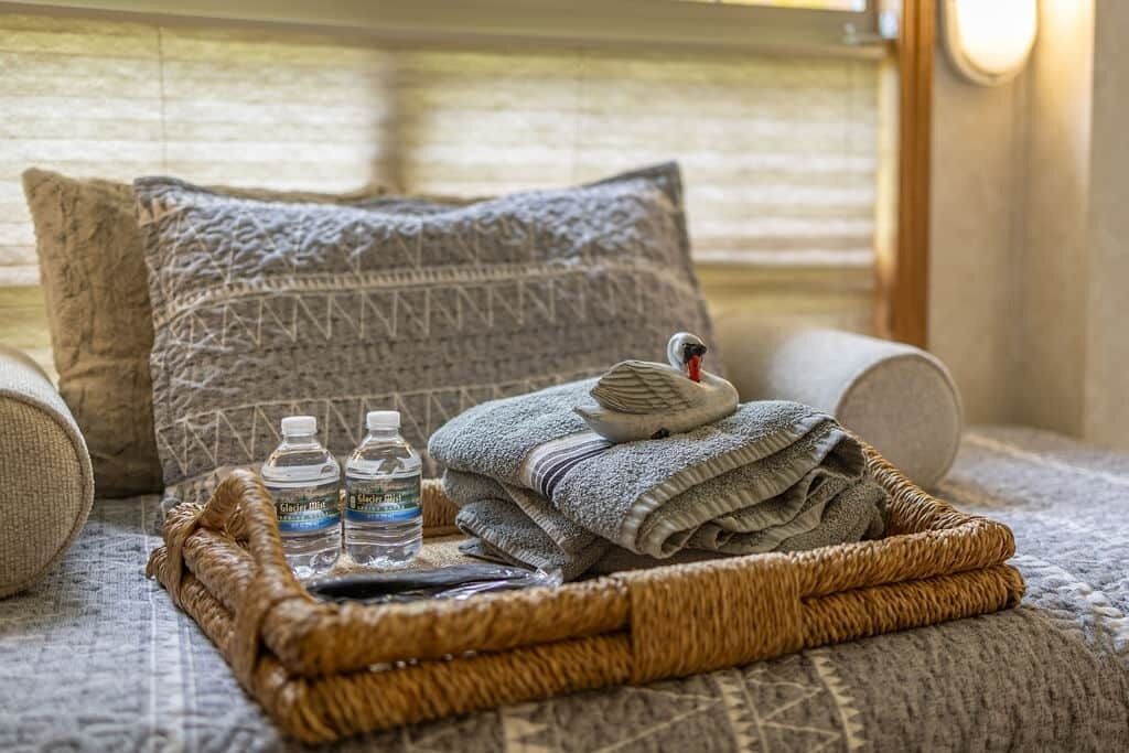 Ein gemütliches Zimmer mit einem Bett, einem gewebten Korb mit Handtüchern und Wasserflaschen sowie einem gemusterten Kissen.