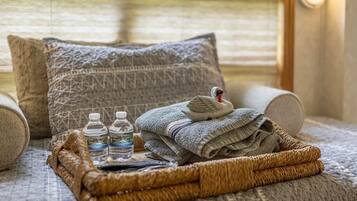 Ein gemütliches Zimmer mit einem Bett, einem gewebten Korb mit Handtüchern und Wasserflaschen sowie einem gemusterten Kissen.