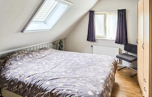 A bedroom with a sloped ceiling, a bed with a leaf-patterned bedspread, a radiator, a desk, and a wardrobe. - Amazing home in Sumar with WiFi (Sumar)