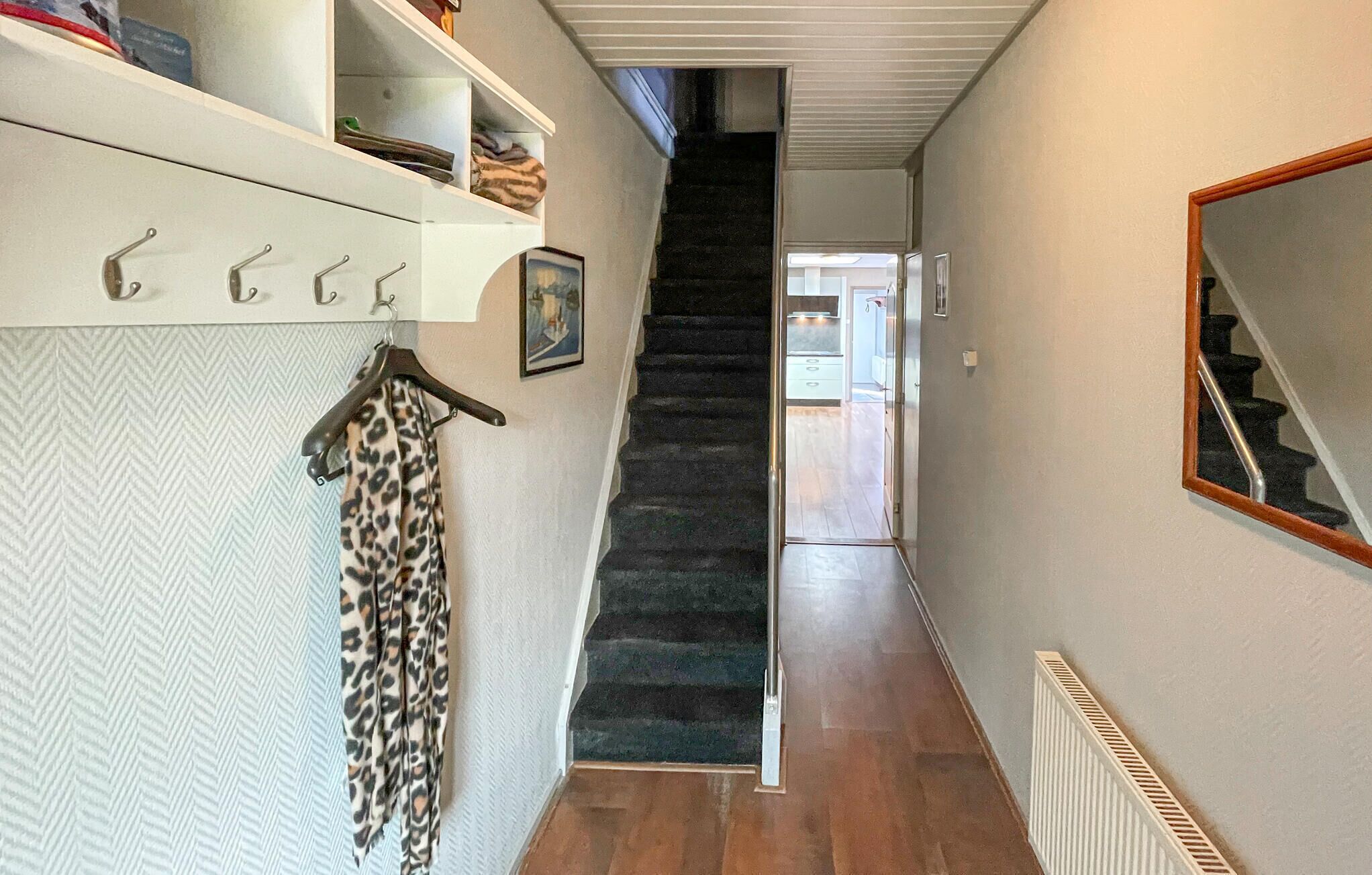 A narrow hallway with a carpeted staircase, a radiator, and a mirror on the wall.
