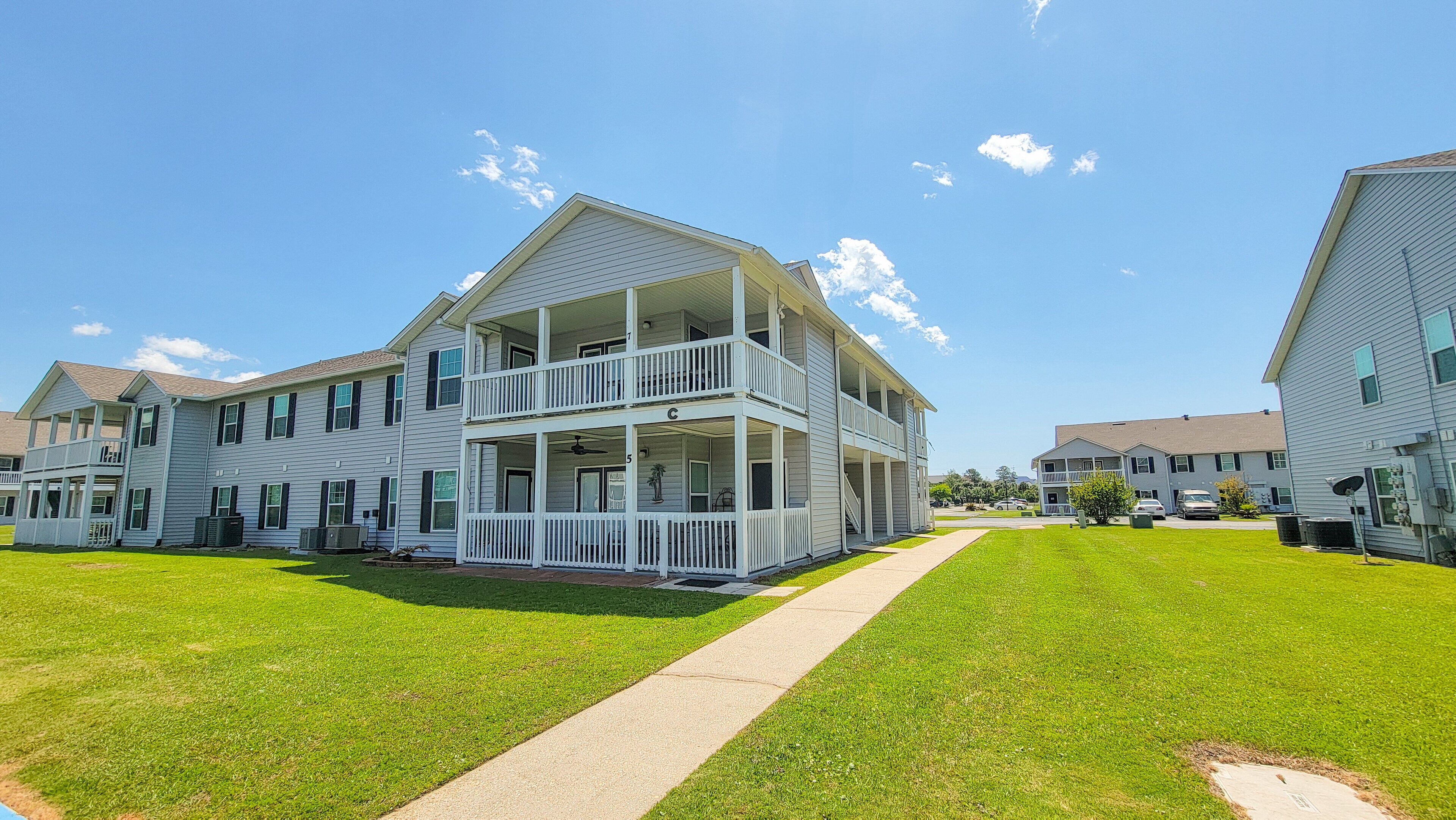 A multi-story residential building with a balcony on the second floor, a covered front porch, and a well-maintained lawn.