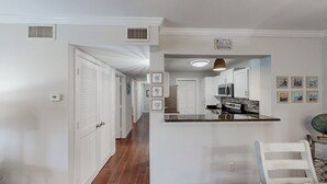 Une cuisine moderne avec des meubles blancs, un plan de travail noir et un four à micro-ondes. On y trouve une pancarte sur laquelle est écrit : « Bienvenue à la maison de plage ».