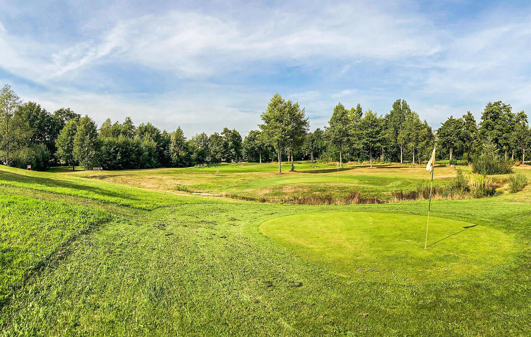 A golf course with well-maintained grass, trees, and a clear sky.
