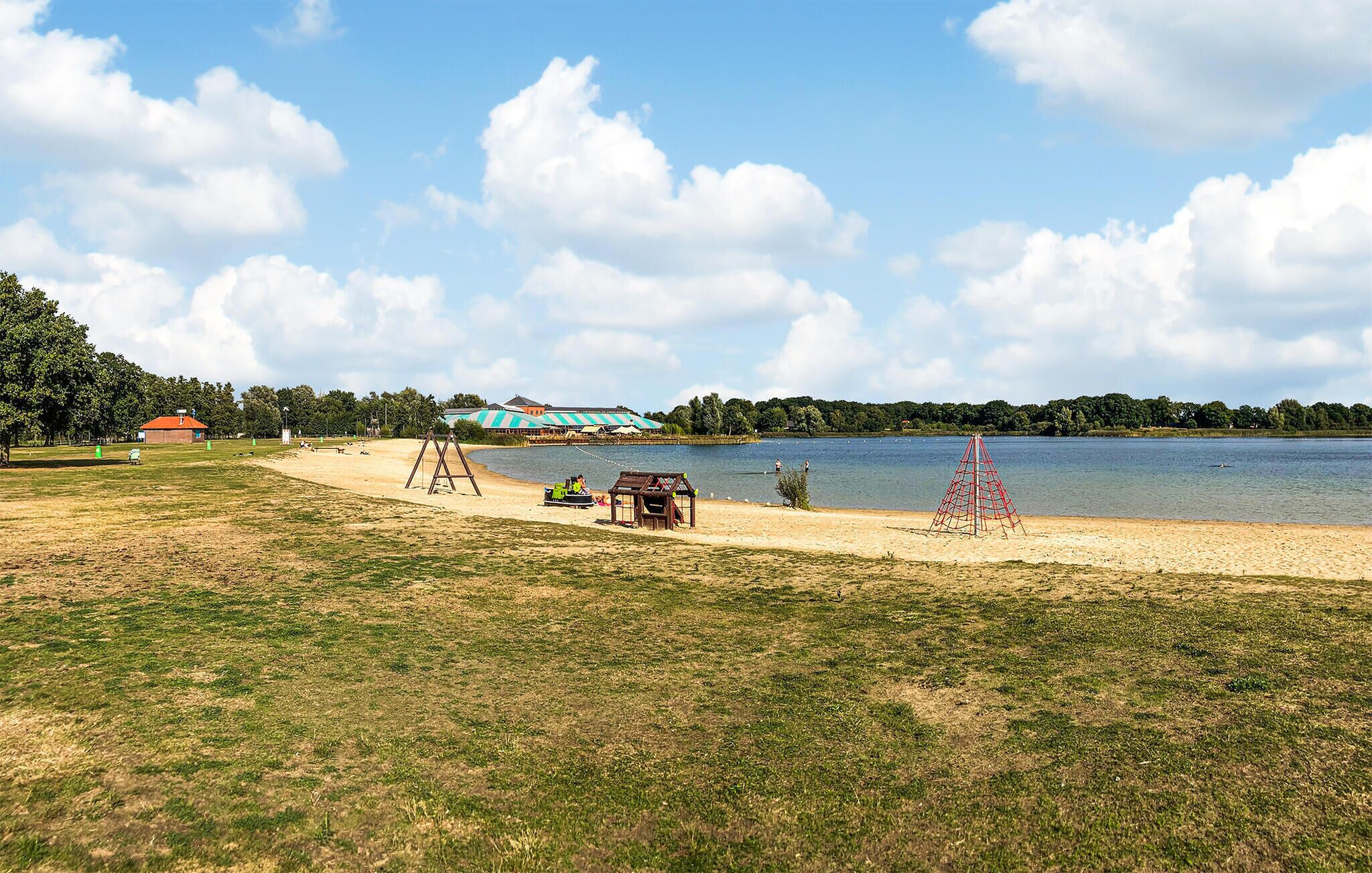 A lakeside park with a sandy beach, a swing set, and a small playhouse.