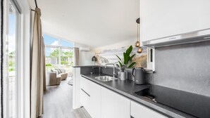 Une cuisine moderne dotée d’un grand îlot central, d’appareils électroménagers en acier inoxydable et offrant une vue sur l’extérieur.