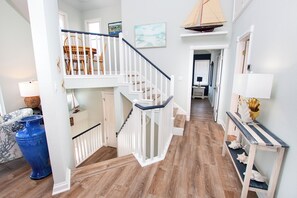Una escalera con barandillas blancas, piso de madera y un área de comedor con sillas y una mesa.