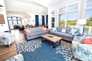 Een ruime woonkamer met een grijze zithoek, een salontafel en een blauw vloerkleed met patroon.