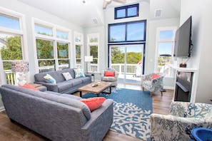 A spacious living room with a gray sofa, a patterned armchair, and a television mounted on the wall.