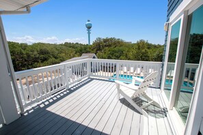 A wooden deck with a pool, white railings, and a view of a tower in the distance.