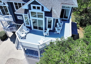 A multi-story house with a deck, multiple windows, and outdoor seating.