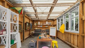 A cozy room with wooden walls, a glass ceiling, a sofa, a table with art supplies, and a small stool. - Nice home in Svaneke with WiFi (Svaneke)