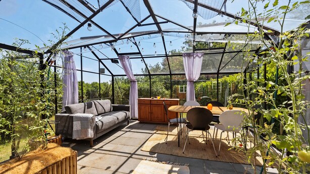 A greenhouse with a sofa, dining table, chairs, and a wooden cabinet. - Nice home in Svaneke with WiFi (Svaneke)