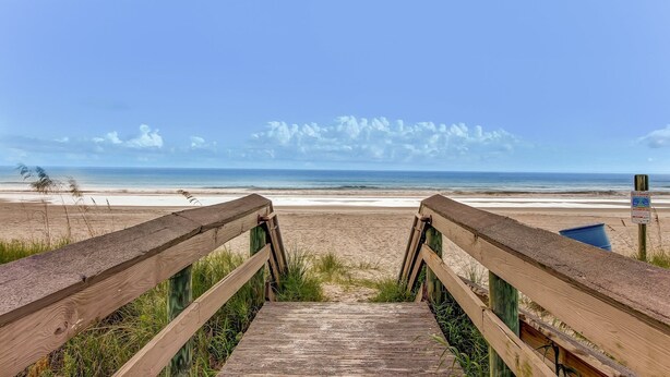 Un paseo marítimo de madera que conduce a una playa, con vista despejada al océano y al cielo.