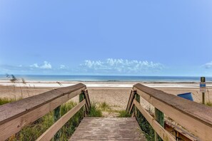 Un paseo marítimo de madera que conduce a una playa, con vista despejada al océano y al cielo.