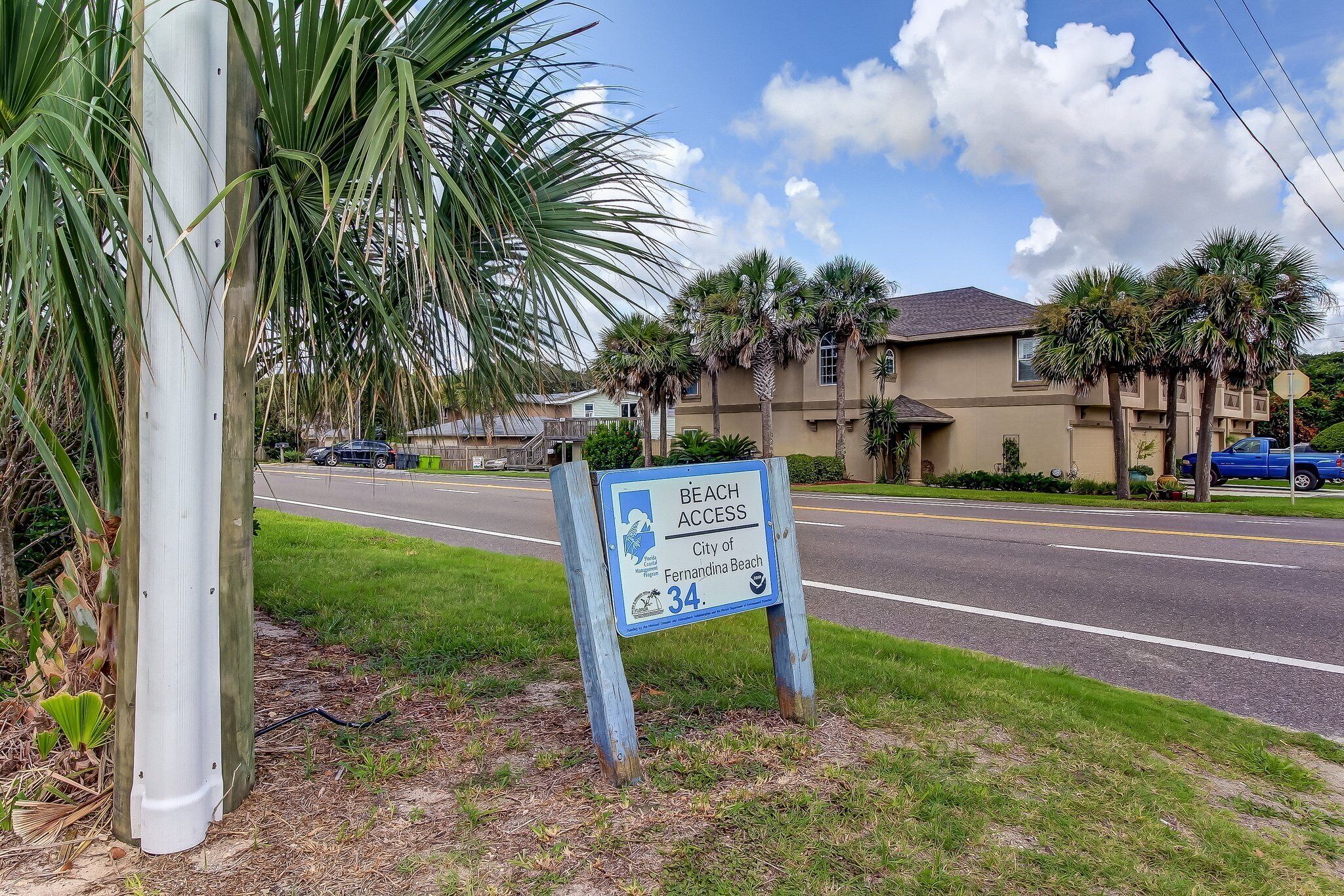 A beach access sign for the City of Fernandina Beach, Florida, with a clear road and residential buildings in the background.