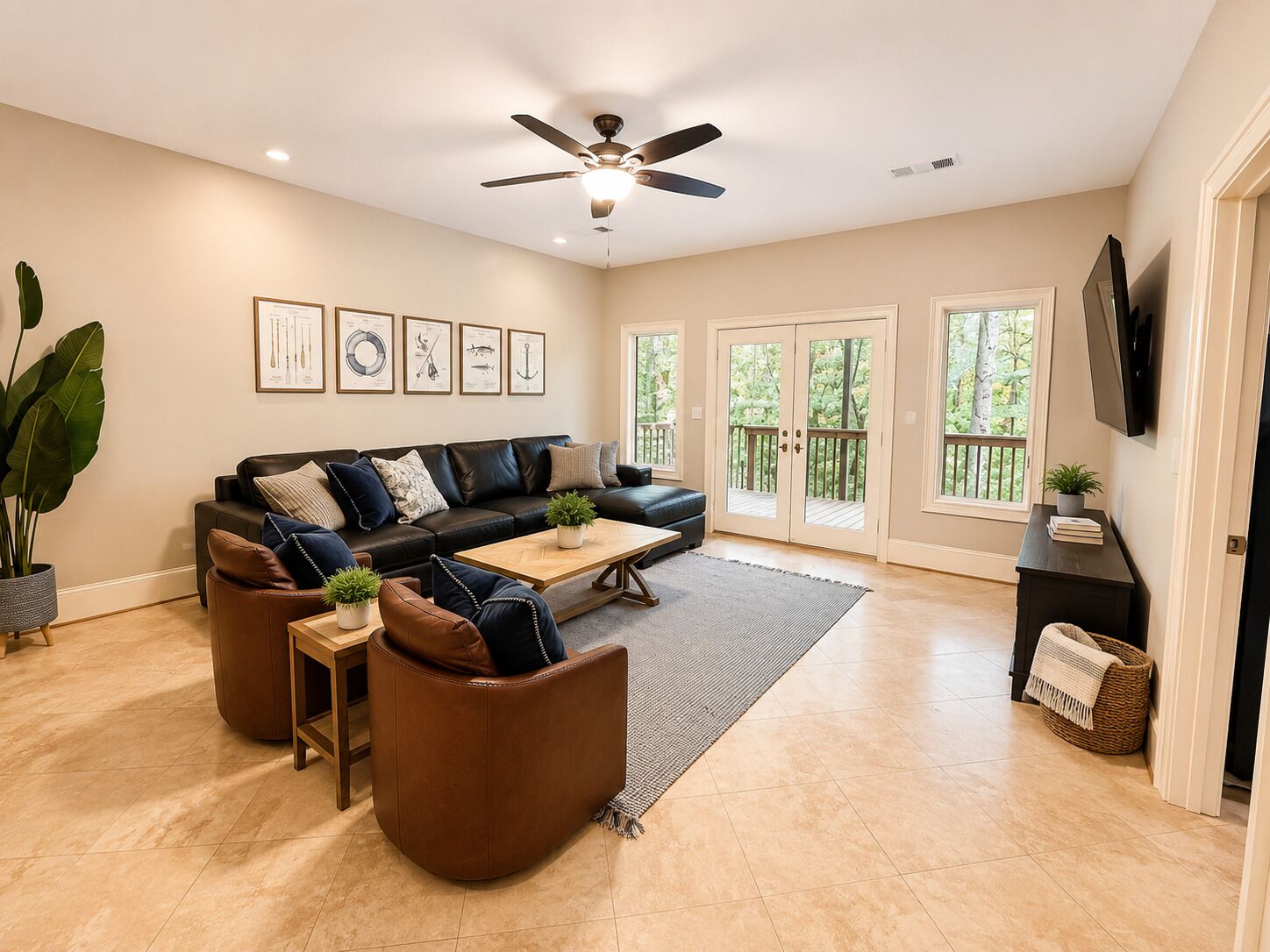 A spacious living room with a black leather sofa, brown leather chairs, a wooden coffee table, and a ceiling fan.