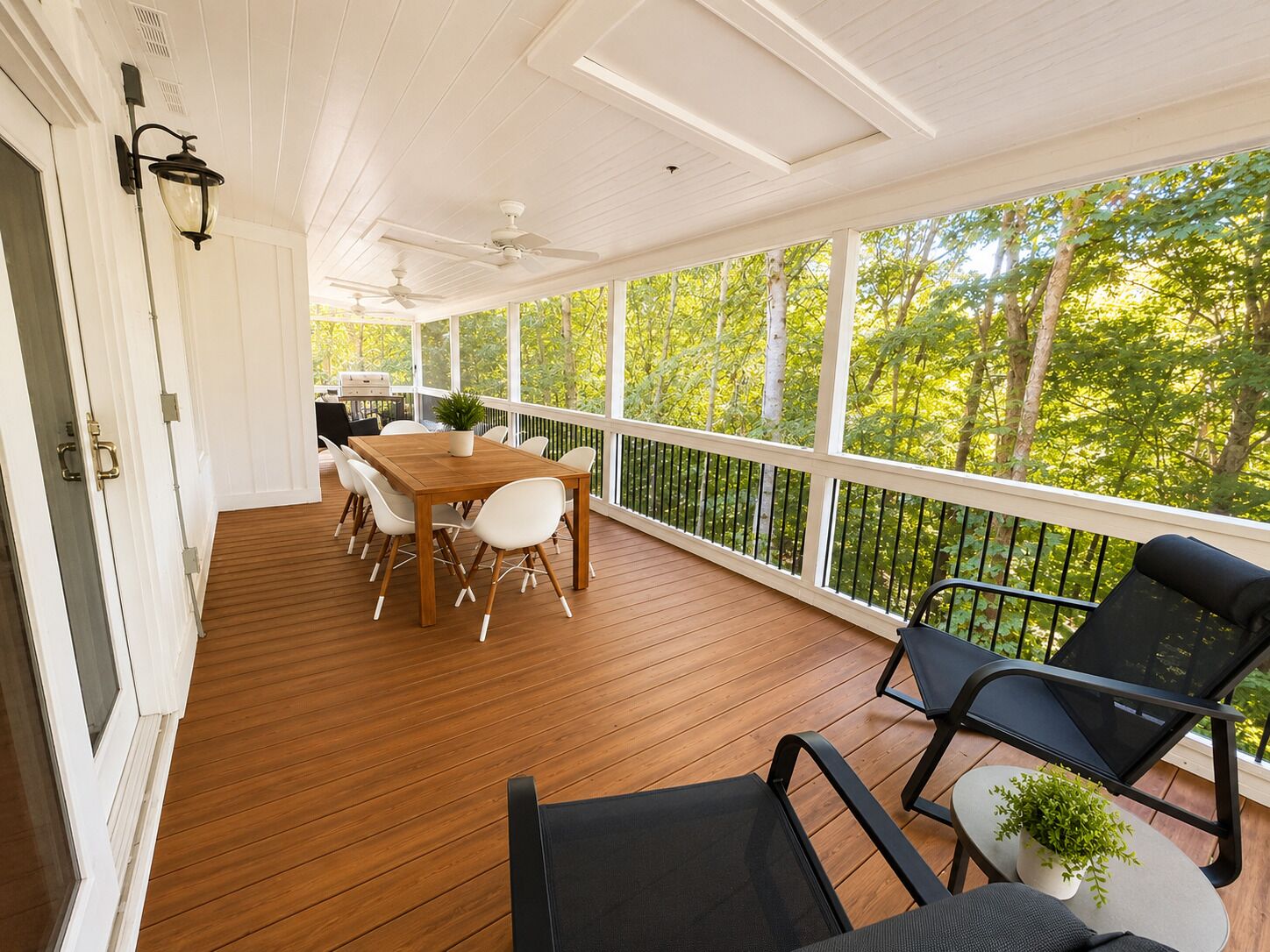 Un espace extérieur abrité doté d’une terrasse en bois, d’une table à manger avec des chaises, d’un barbecue et d’une vue sur les arbres.