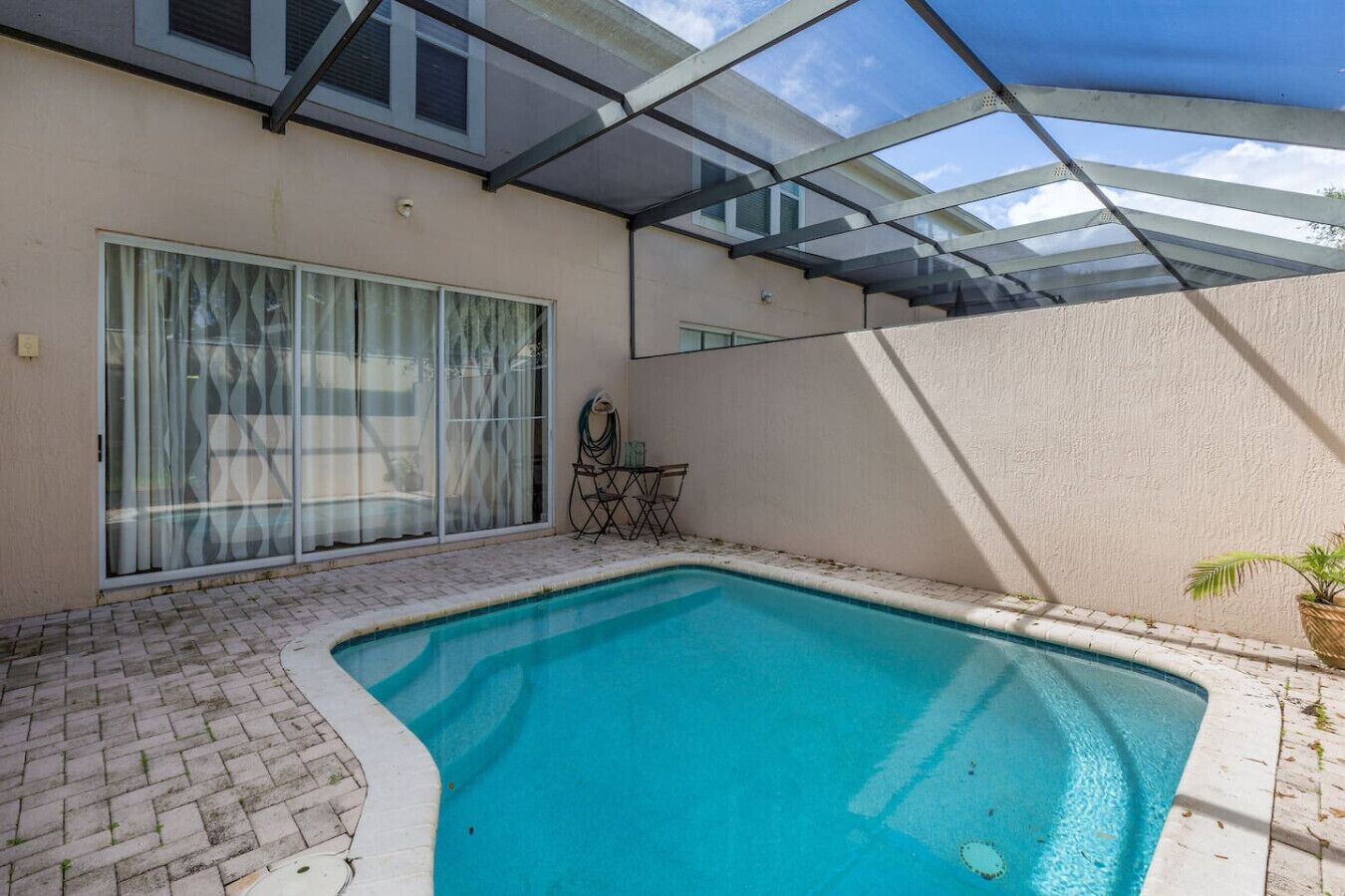 A swimming pool with a glass enclosure, a sliding glass door, and a small table with chairs.