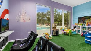 Ein Zimmer mit Blick auf einen Pool, ein Spielbereich mit Spielzeug und ein Wandgemälde mit einem Schloss.