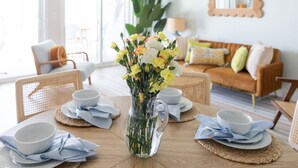 Una mesa de comedor con una jarra de vidrio transparente llena de flores, platos blancos y servilletas azules.