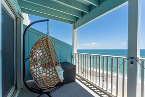A balcony with a hanging chair, a view of the ocean, and a white railing.