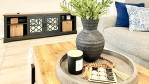 A living room with a TV mounted on the wall, a wooden coffee table with a vase and decorative items, and a grey sofa with blue cushions. - Luxe & Modern Home-10 min to Disney Parks+Heated Pool+ Pets allowed (Kissimmee)