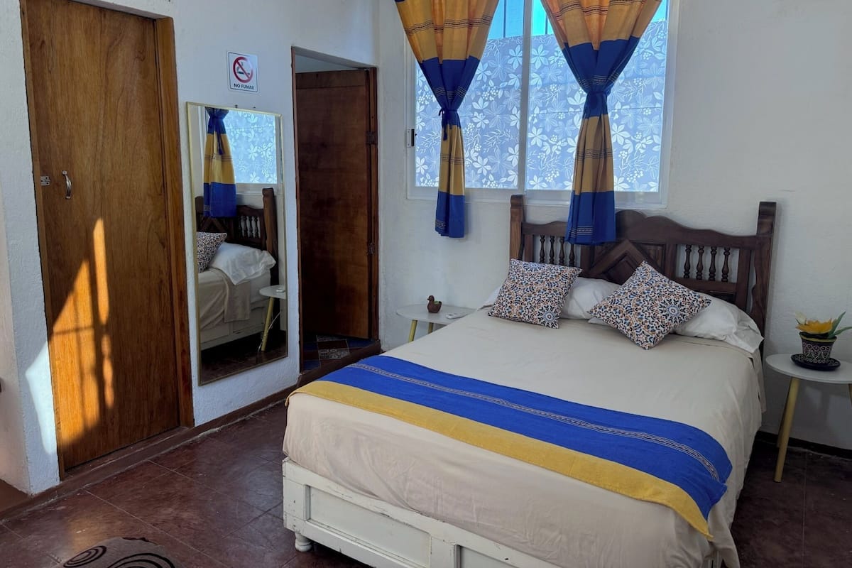 Un dormitorio con cama, cortinas, armario, una mesita y una ventana.