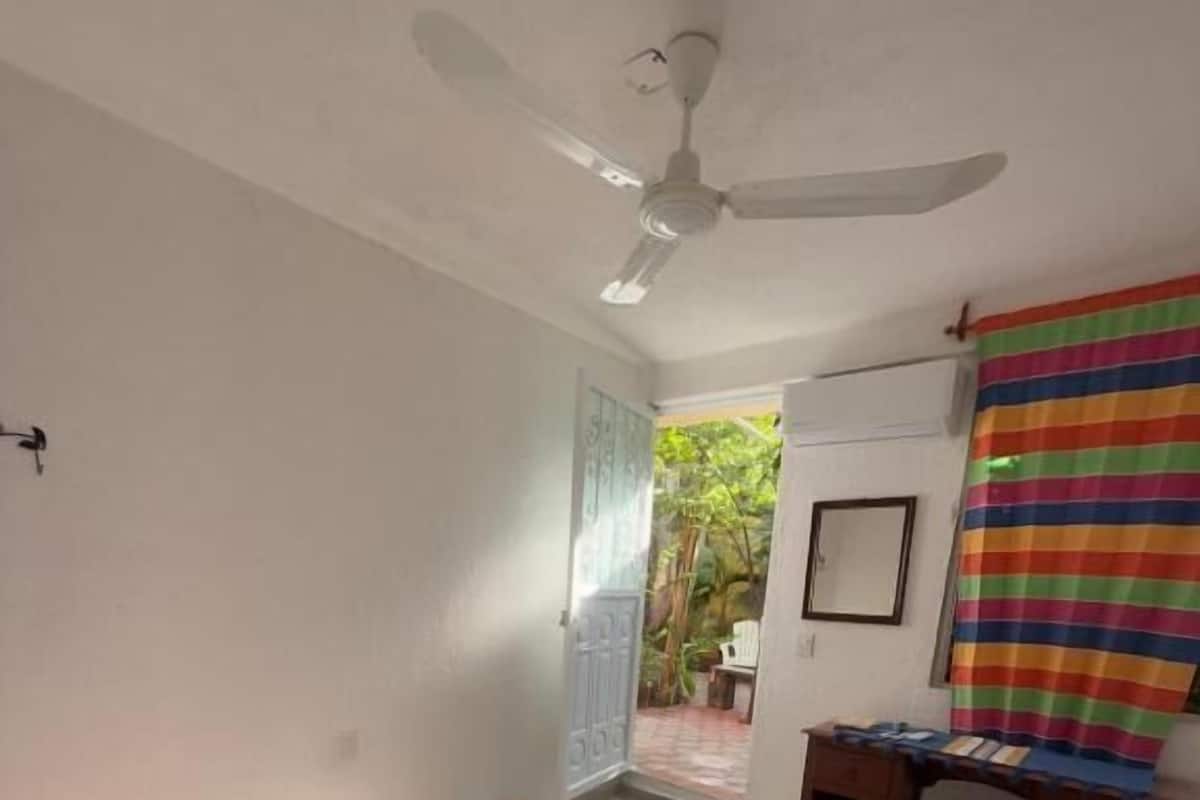 Un dormitorio con cama, escritorio, silla, ventilador de techo y vistas al exterior.