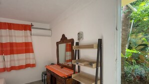 A room with a bed, a desk, a mirror, and a shelf. There is a window with a view of greenery outside. - Casa Icaco  (Puerto Escondido)