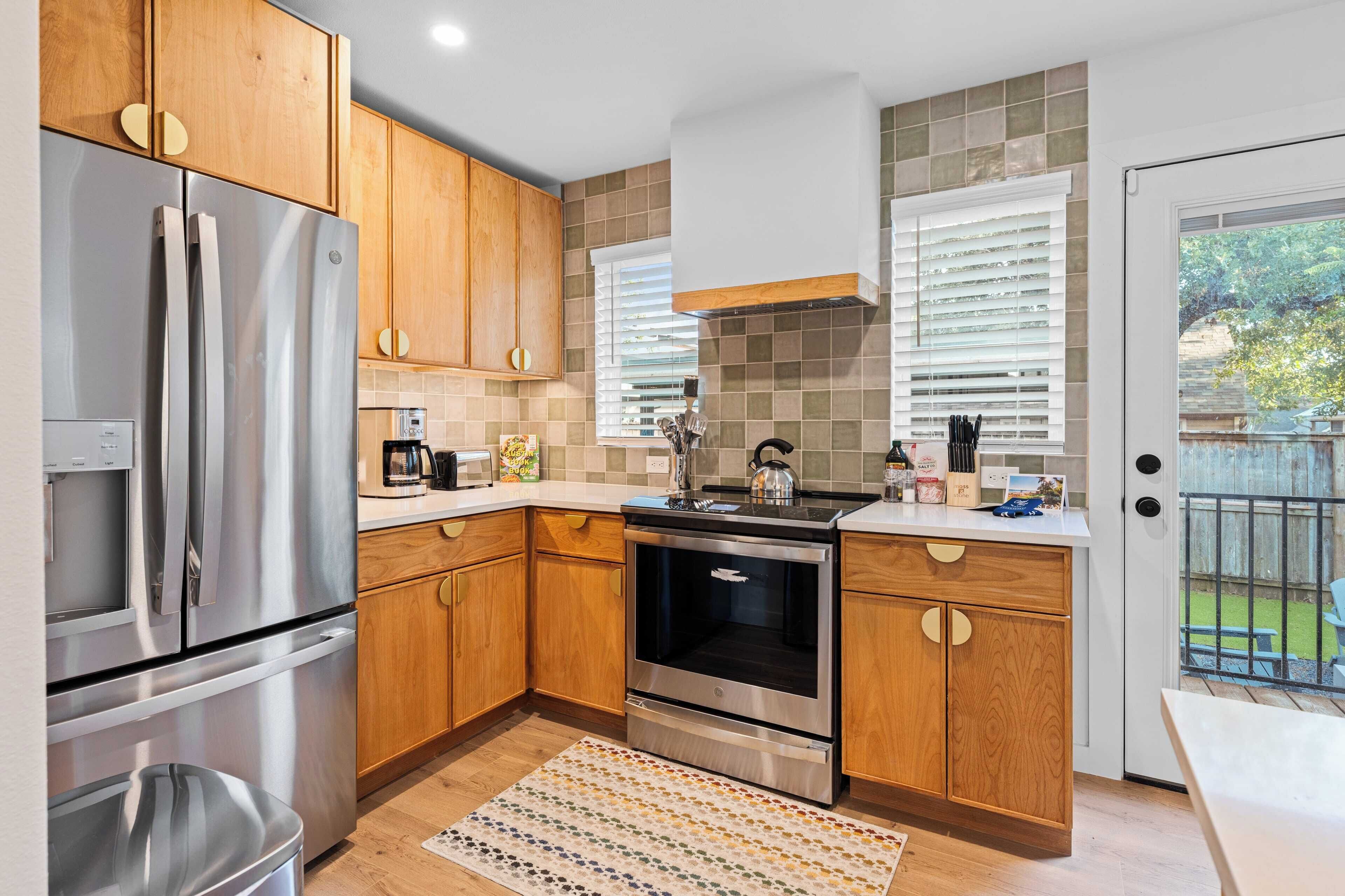 A modern kitchen with wooden cabinets, stainless steel appliances, and a view of the backyard through a sliding glass door.