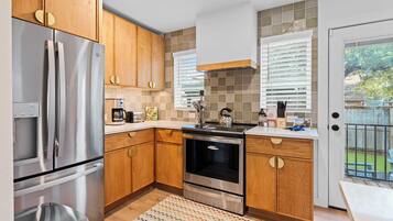 A modern kitchen with wooden cabinets, stainless steel appliances, and a view of the backyard through a sliding glass door.