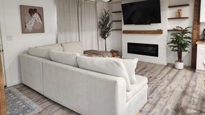 A living room with a sofa, a ceiling fan, a TV, a fireplace, and a plant. - Spacious 4BR Home, Screened Porch, Fenced Yard, Pet-Friendly, 7 Min to Benning (Columbus)
