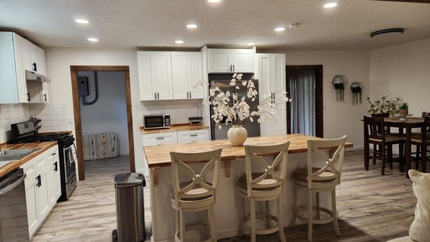 A modern kitchen with white cabinets, a wooden island with bar stools, a microwave, and a stainless steel trash can. - Spacious 4BR Home, Screened Porch, Fenced Yard, Pet-Friendly, 7 Min to Benning (Columbus)
