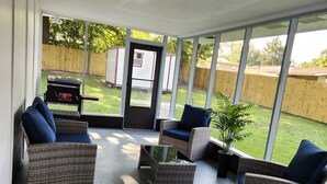 A covered patio with wicker furniture and a grill in the background. - Spacious 4BR Home, Screened Porch, Fenced Yard, Pet-Friendly, 7 Min to Benning (Columbus)