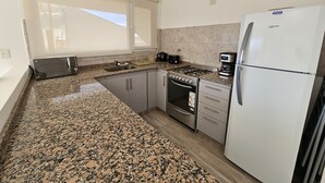 A kitchen with granite countertops, a gas stove, a built-in oven, a refrigerator, and a window with blinds. - Andina View Bariloche (San Carlos de Bariloche)