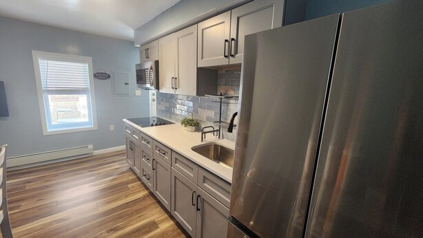 A modern kitchen with stainless steel appliances, light grey cabinets, and a wooden floor.
