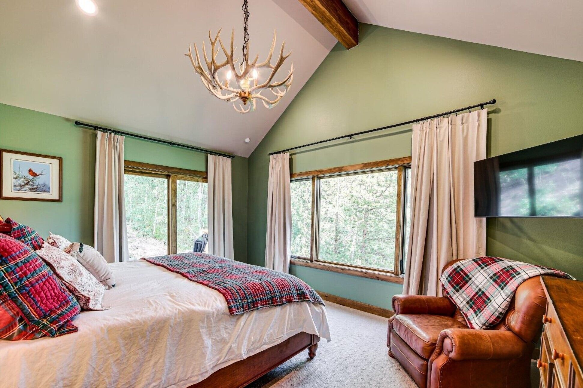 A bedroom with a large bed, a leather armchair, a chandelier, and a TV mounted on the wall.