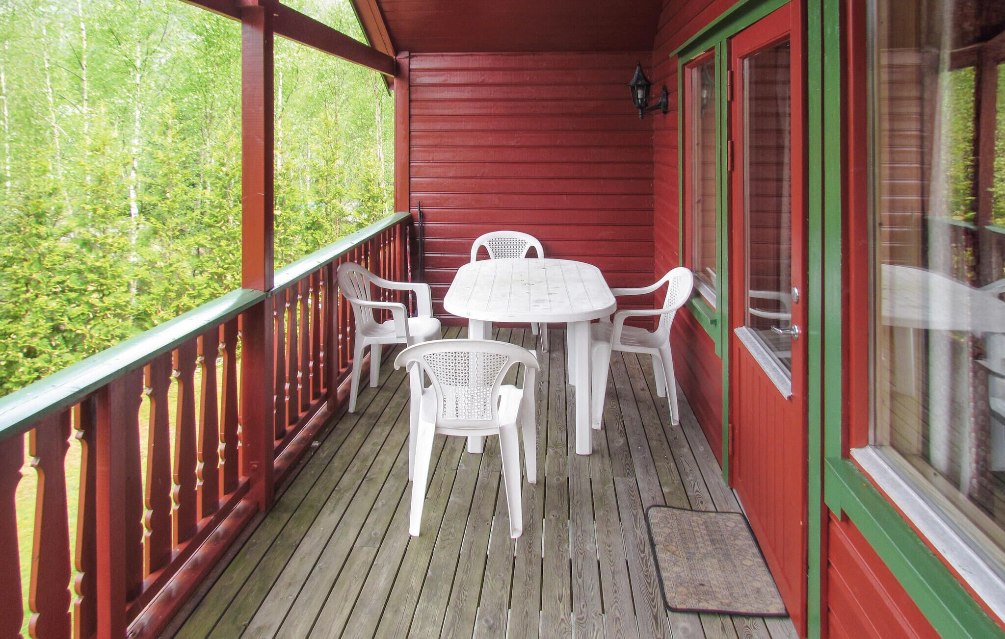 A wooden deck with a red railing, a white table, and four white chairs.