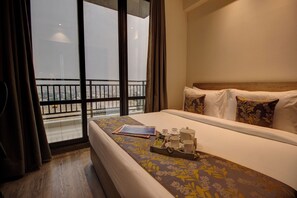 A hotel room with a bed, a window with curtains, a balcony, and a tray with breakfast items.