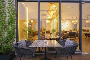 An indoor dining area with wicker chairs, a marble table, and pendant lighting. - Rhythm Gurugram - Hotel & Suites (GURUGRAM)