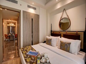 A hotel room with a bed, a dining area, and a mirror on the wall. - Rhythm Gurugram - Hotel & Suites (GURUGRAM)