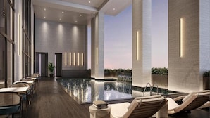 Un área interior de piscina moderna con sillones de descanso, una mesa larga y una cascada.